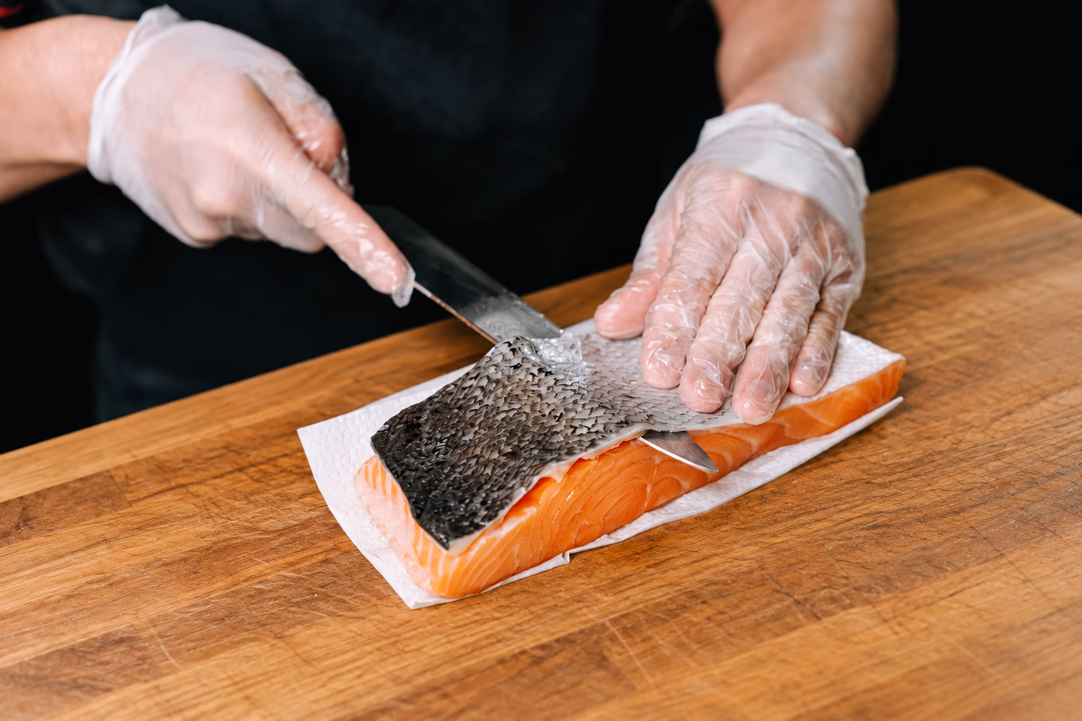 Chef removing skin from a salmon fillet on a wooden board