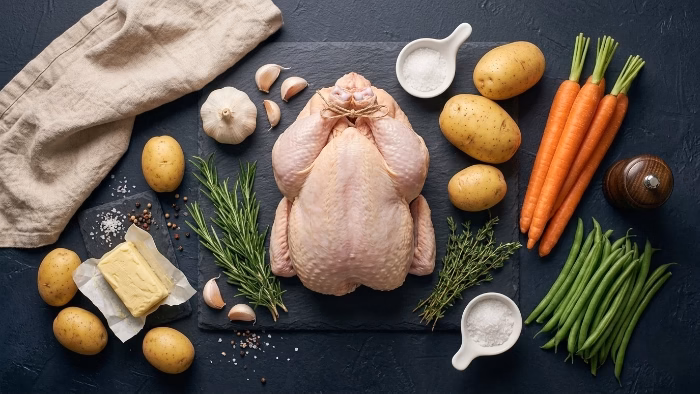 sunday dinner ingredients: whole chicken, potatoes, carrots and fresh herbs